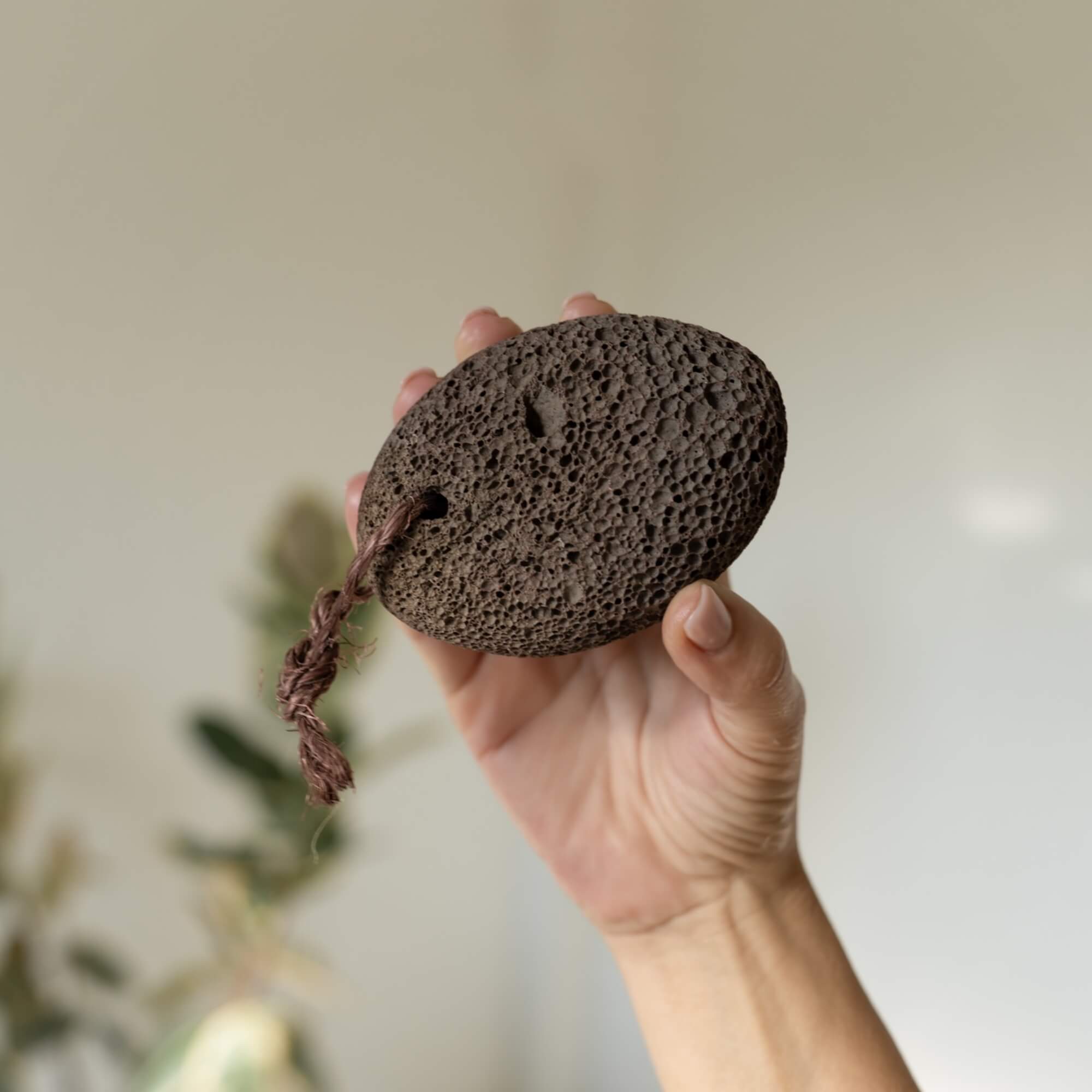 Dunkler natürlicher Bimsstein mit Kordel in der Hand zur Entfernung von Hornhaut